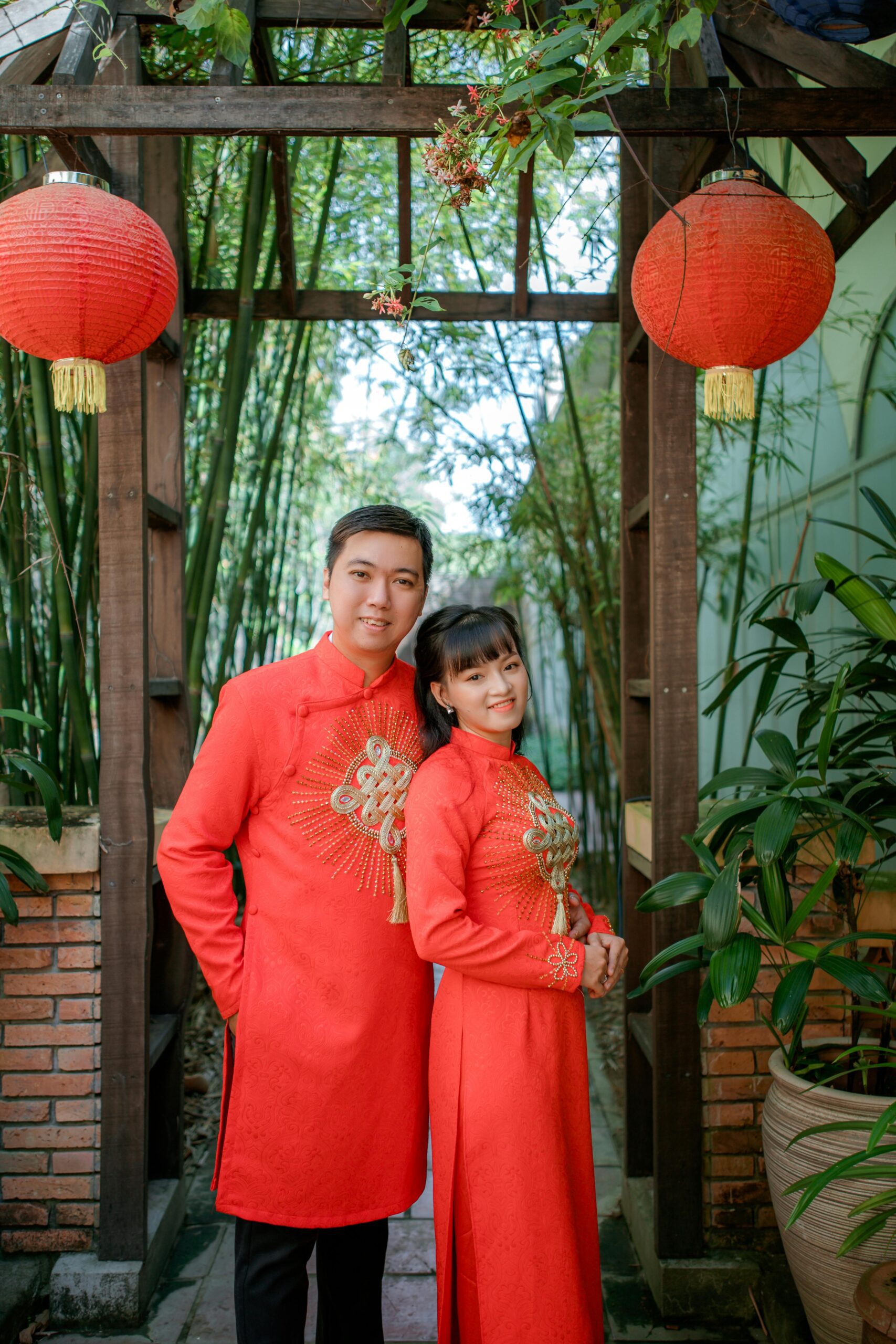 A happy couple in vibrant traditional clothing posing with red lanterns.
