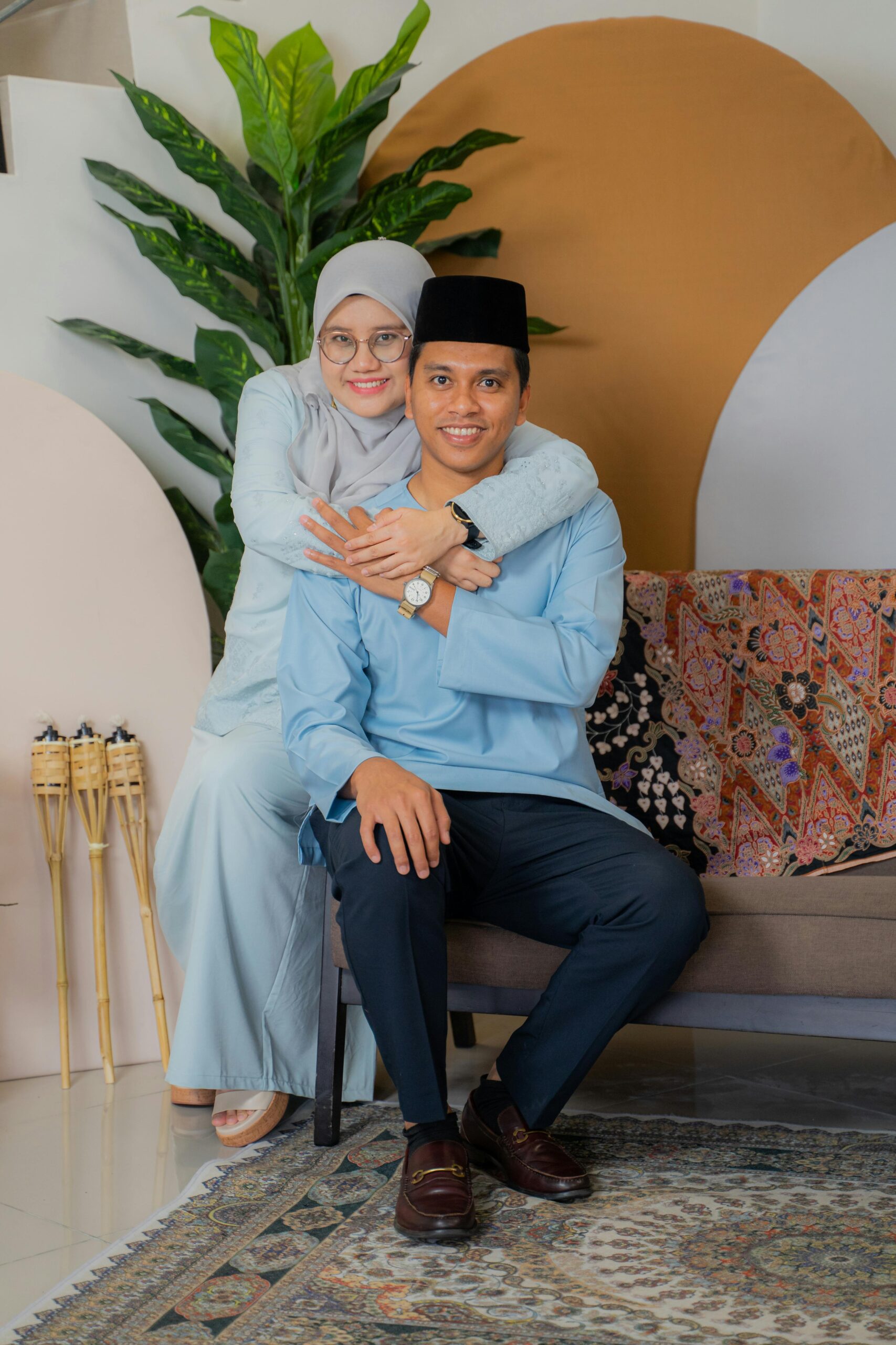 Smiling couple in traditional attire posing indoors with decorative backdrop.